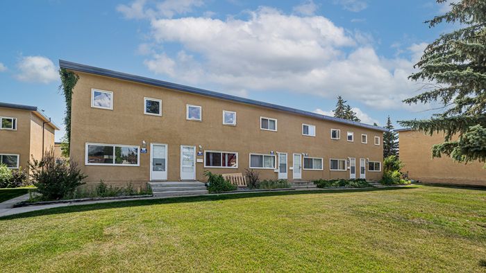 Charming townhouse with a modern facade, lush green lawn, and picturesque sky views, perfect for serene living.