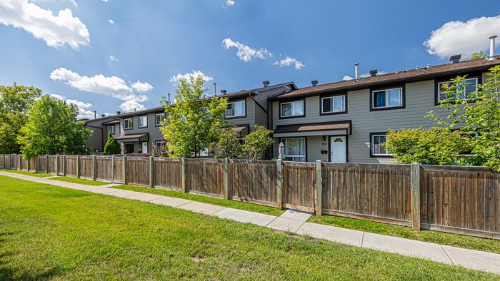 Charming row of townhouses with well-maintained lawns and vibrant greenery under a bright blue sky.