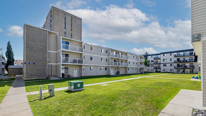 Bright, open apartment complex with well-maintained grassy courtyard and modern balconies, ideal for comfortable urban living.