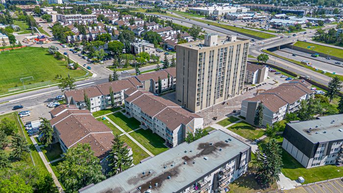 Vibrant aerial view of modern apartment complex surrounded by lush green spaces and easy highway access, perfect for convenient urban living.