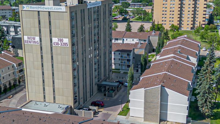 Aerial view of a modern apartment complex featuring spacious units and lush green surroundings, now available for rent. The main building stands tall with a prominent 'Now Renting' sign, highlighting its prime location and convenient amenities.