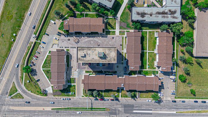 Aerial view of a modern apartment complex showcasing neatly arranged buildings, well-maintained green spaces, and ample parking facilities at a bustling intersection.