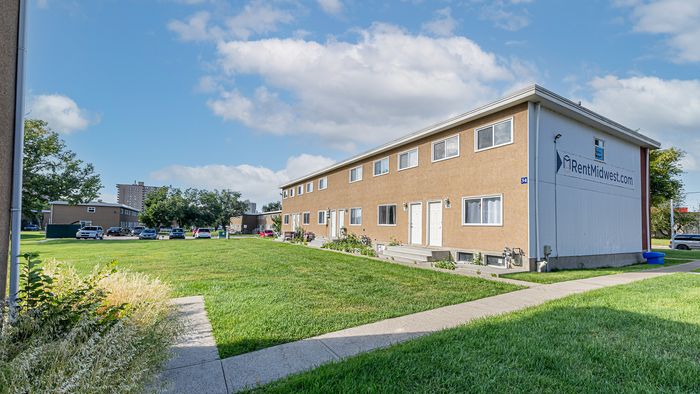 Spacious apartment complex with beautiful exterior showcasing a well-maintained grassy lawn under a clear blue sky.