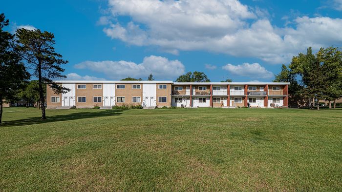 Charming two-story apartment complex with a spacious green lawn and scenic sky, offering a tranquil living environment.