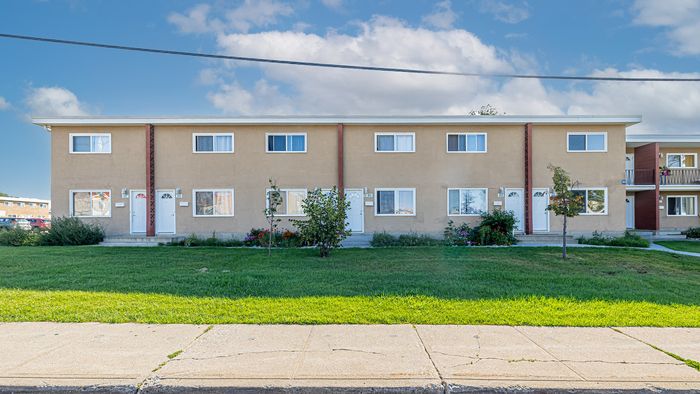 Charming multi-unit apartment building with welcoming entrance, lush green lawn, and abundant natural light through large windows.