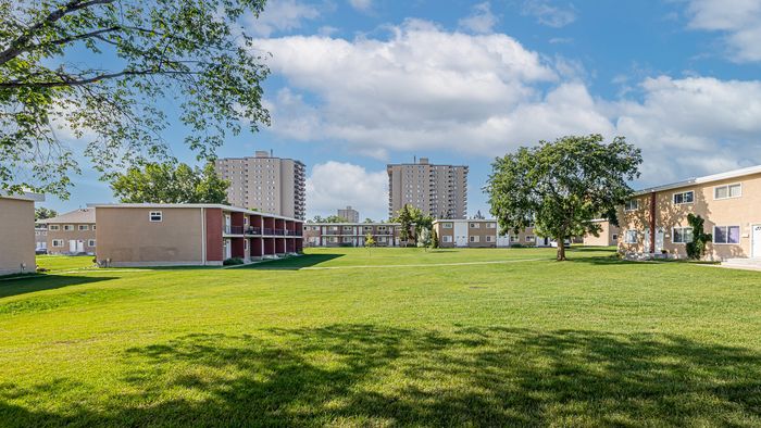 Scenic apartment complex surrounded by lush greenery and open space, featuring modern low-rise buildings and a vibrant community atmosphere under a clear blue sky.