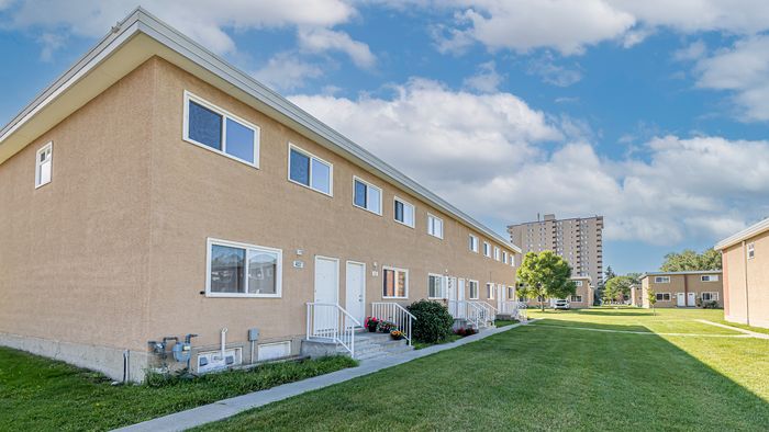 Charming townhouse complex with manicured lawns, vibrant flower beds, and clear blue skies, ideal for serene living.