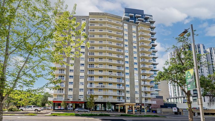 Modern high-rise apartment building with spacious balconies, surrounded by lush greenery and vibrant urban life.