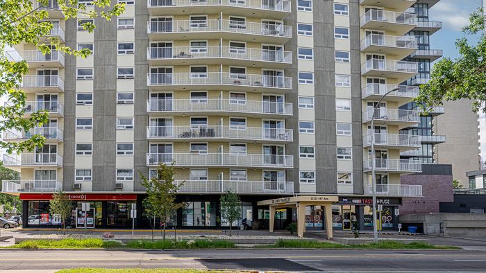 Modern high-rise apartment building with spacious balconies, retail shops on ground level, and lush green surroundings.