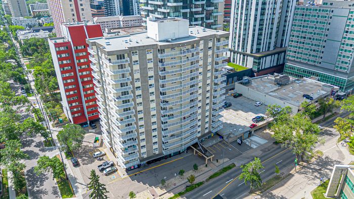 Aerial view of a modern high-rise apartment building surrounded by lush greenery, showcasing vibrant city living with ample parking and proximity to urban amenities.