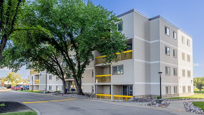 Modern apartment building with vibrant yellow accents, surrounded by lush greenery, offering a refreshing and welcoming atmosphere.