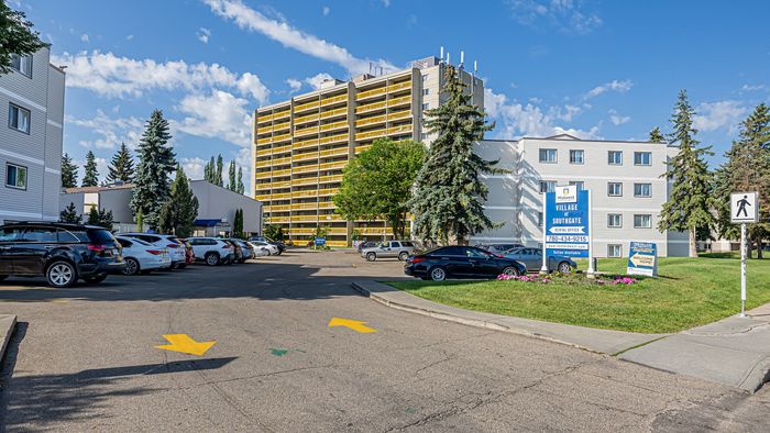 Charming apartment complex with distinctive yellow balconies, surrounded by lush greenery and ample parking in a serene neighborhood.