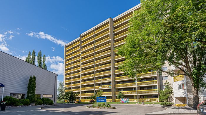 Contemporary apartment building with vibrant yellow balconies surrounded by lush greenery, basking under a clear blue sky.