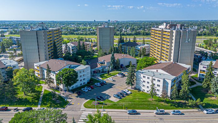 Vibrant aerial view of a lush residential community surrounded by greenery, showcasing multiple apartment buildings under a clear blue sky.