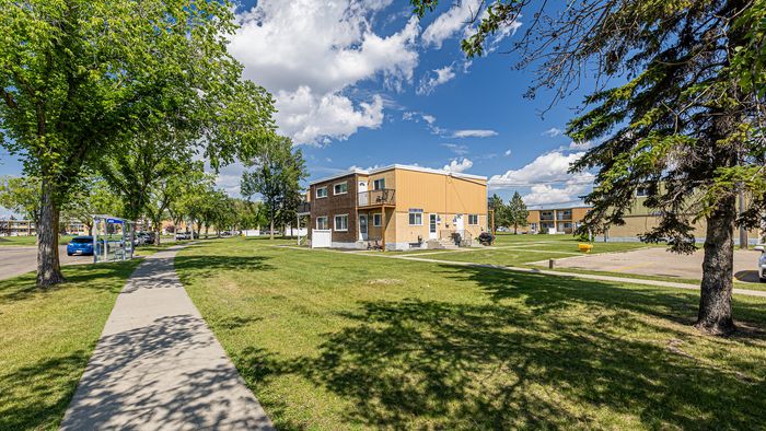 Inviting suburban apartment building surrounded by lush green lawns and mature trees under a clear blue sky.