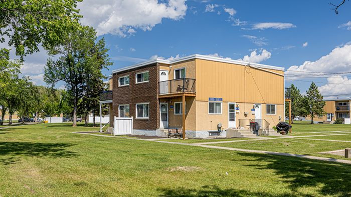 Charming two-story building with a mix of brick and mustard siding, nestled in a lush, green neighborhood under a vibrant blue sky.