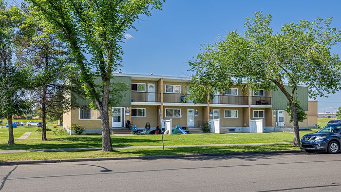 Charming two-story apartment complex surrounded by lush greenery, featuring spacious balconies and ample parking space.