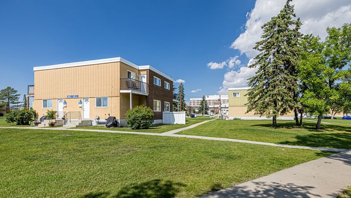 Charming apartment building with a sunny exterior, surrounded by lush green lawns and mature trees. Perfect for those seeking tranquil suburban living.
