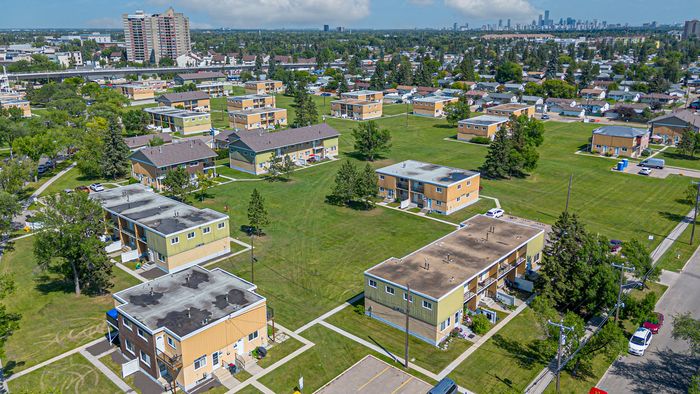 Charming suburban community with spacious green lawns and multiple modern apartment buildings set against a vibrant city skyline.