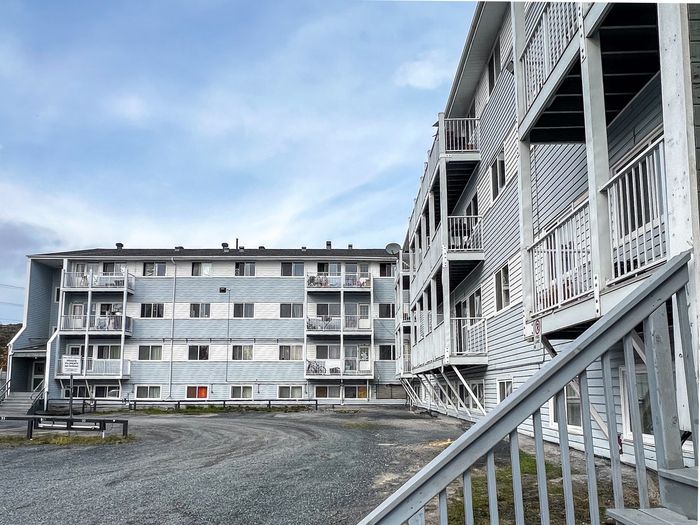 Bright and welcoming four-story apartment building with charming balconies and a spacious gravel driveway, offering comfortable community living.