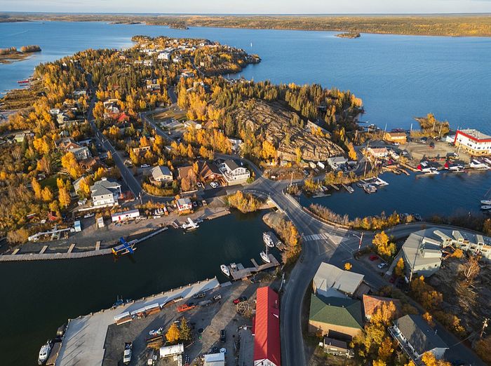 Breathtaking aerial view of a scenic coastal town, surrounded by vibrant autumn foliage, nestled by a tranquil, expansive blue lake.