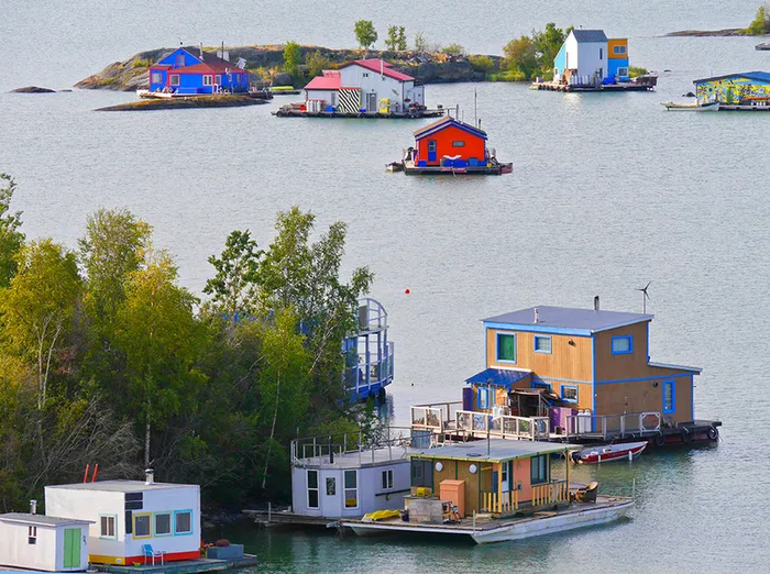 Charming floating homes with vibrant colors nestled on a tranquil lake, surrounded by lush greenery and serene water views.