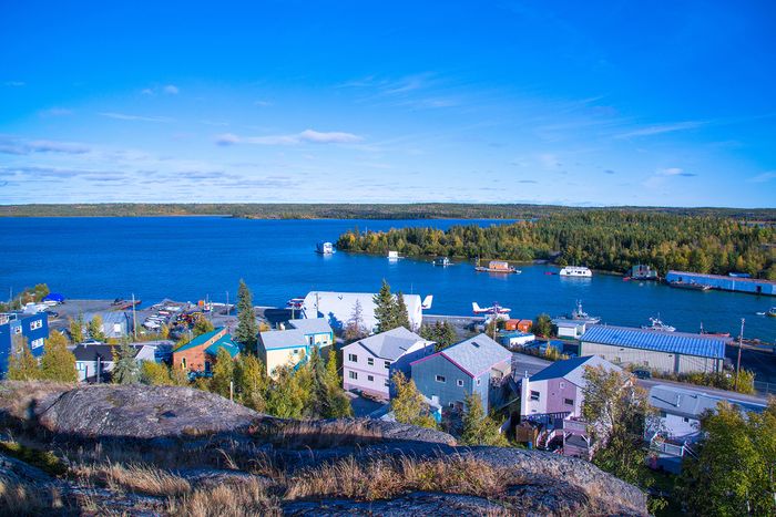 Vibrant lakeside community with colorful houses, serene blue waters, and lush green forest backdrop, perfect for nature lovers.