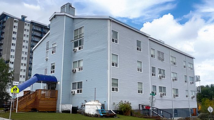 Charming three-story residential building with modern siding, ample windows, and a cozy entrance with a covered awning. Surrounded by greenery, it offers a welcoming neighborhood feel.