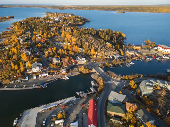 Scenic aerial view of a charming waterfront village surrounded by autumn foliage, serene blue waters, and cozy homes nestled among lush greenery.