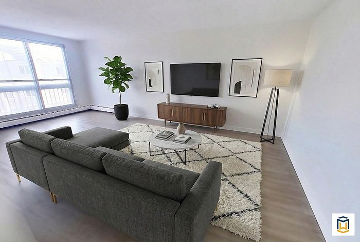 Contemporary living room with stylish gray sectional sofa, large TV, sleek wooden console, and abundant natural light from expansive windows.