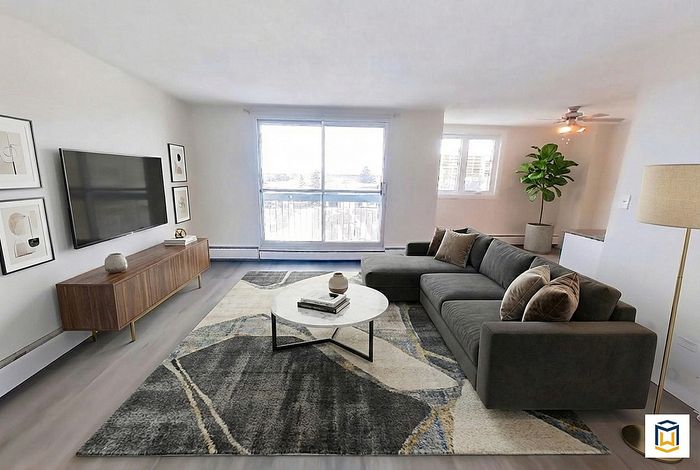 Bright and modern living room with a plush gray sectional, chic rug, and large TV, offering a cozy and stylish space for relaxation.