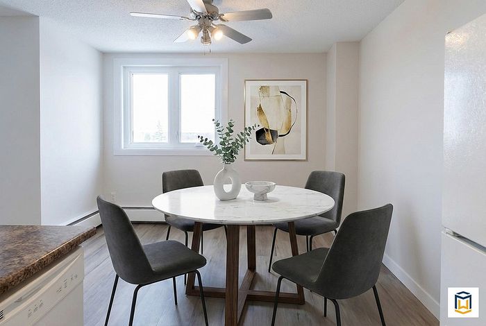 Bright dining area with modern decor featuring a round marble table, sleek gray chairs, and minimalist artwork under a ceiling fan.