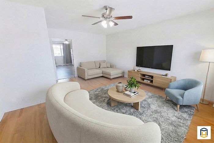 Modern living room with plush furnishings, featuring a curved sofa, chic armchair, and sleek TV setup on a stylish wooden stand beneath a ceiling fan.