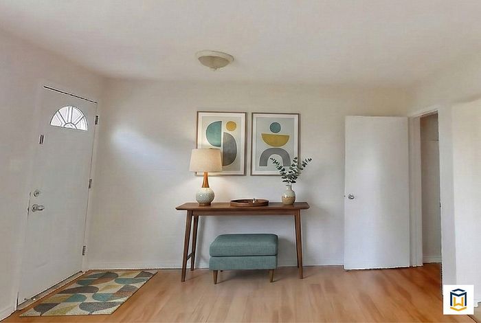 Charming entryway featuring elegant console table, decorative art, and cozy stool on polished hardwood floor.