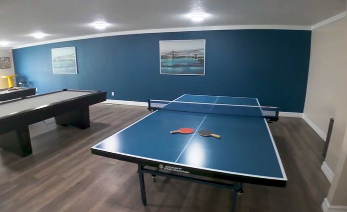 Spacious recreation room featuring a ping pong table and a billiards table, accented by elegant lighting and modern artwork on deep blue walls.