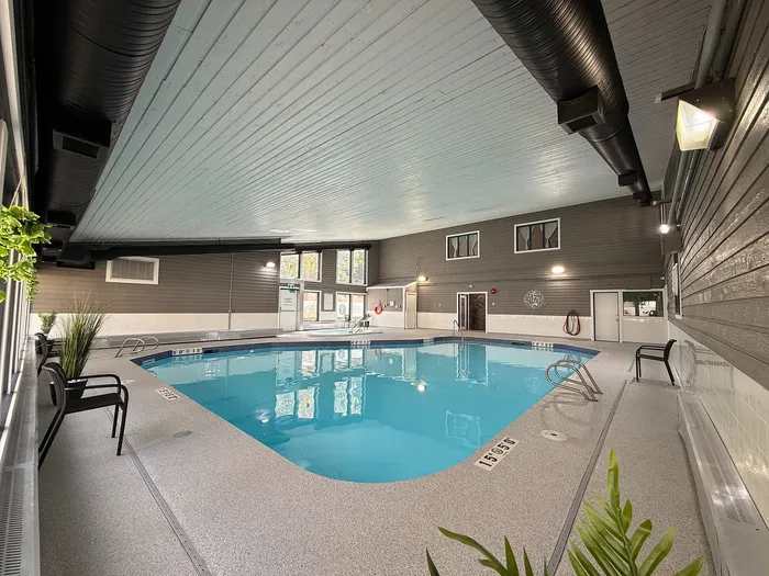 Elegant indoor swimming pool area with modern lighting, cozy seating, and lush green plants, offering a tranquil escape for residents.