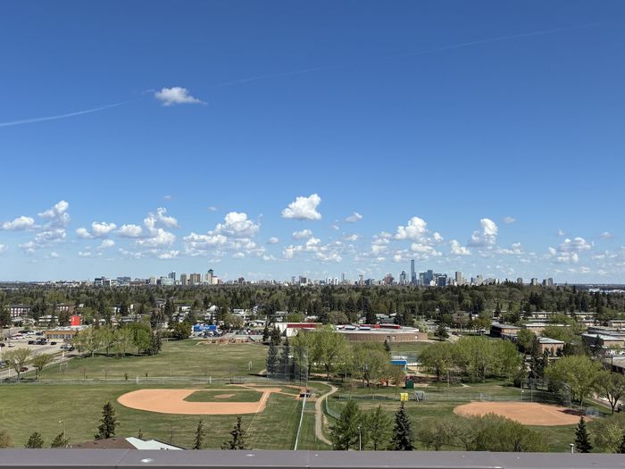Scenic view of a vibrant city skyline against a clear blue sky, overlooking lush green parks and baseball fields.