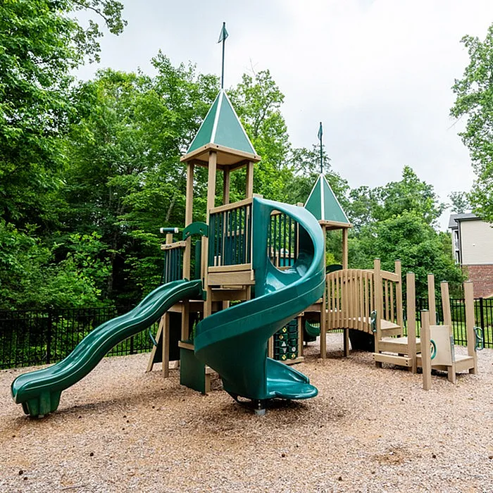 Captivating playground with green slides and wooden structures surrounded by lush trees.