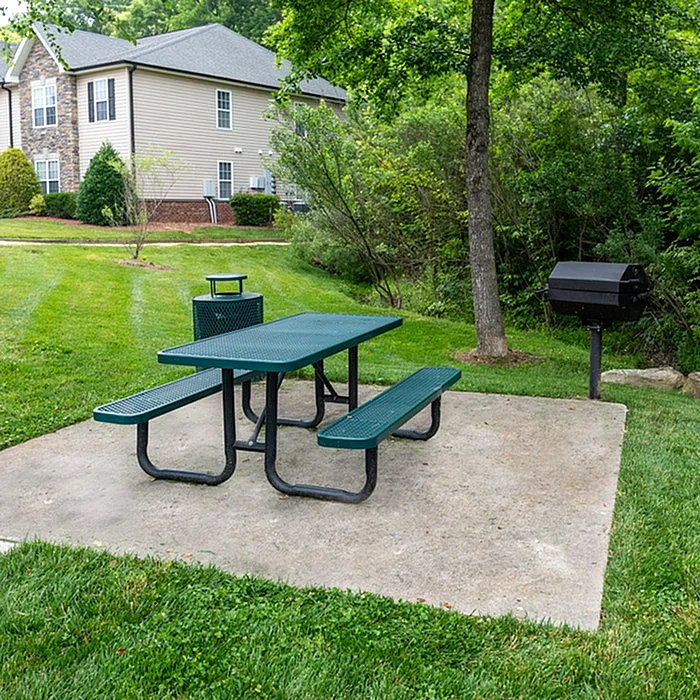 Serene outdoor space with picnic table and grill set against lush greenery and residential backdrop.
