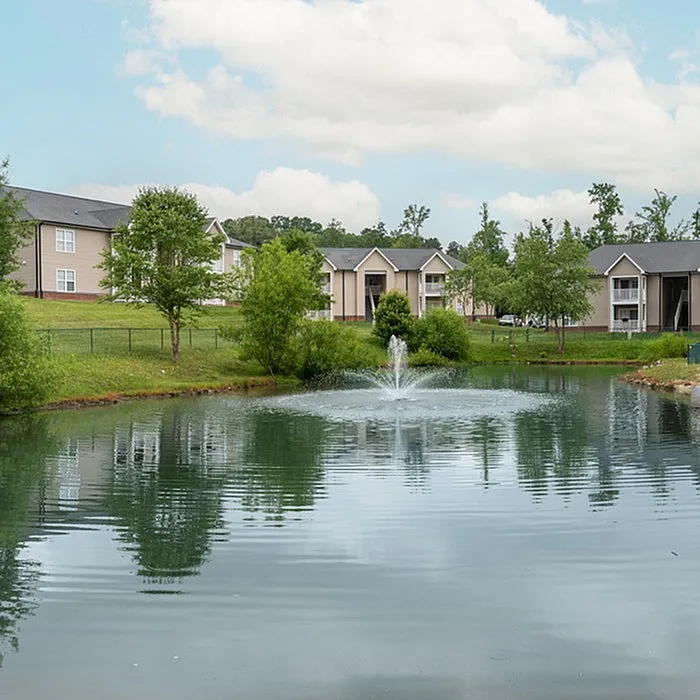 Serene pond with a fountain surrounded by modern apartment buildings and lush greenery.