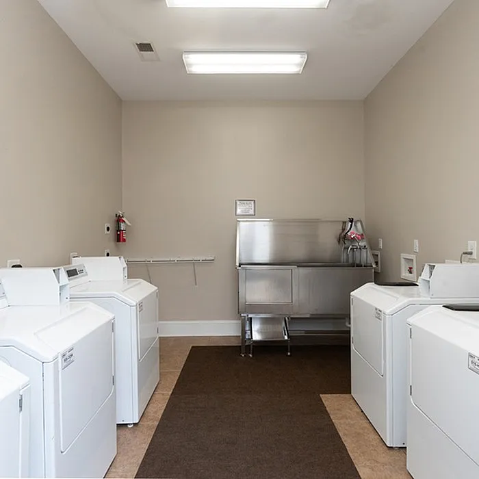 Well-lit laundry room with modern washers and dryers, featuring stainless steel folding station.