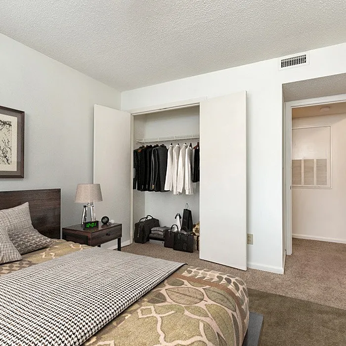 Modern bedroom featuring a neatly organized open closet with clothes and a stylish bed with patterned bedding.