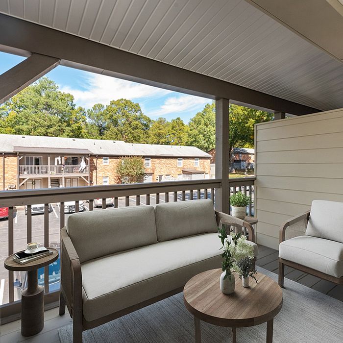 Cozy balcony with neutral furnishings and a serene view of a tree-lined courtyard.