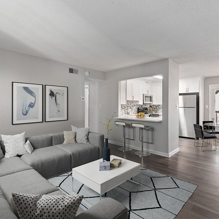 Modern apartment with a sleek gray sofa, bright kitchen, and elegant dining area in an open-concept design.