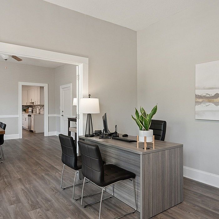 Sophisticated home office with a modern desk, black chairs, and a view into a stylish kitchen.