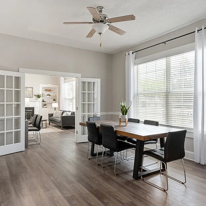 Bright dining area with modern table, stylish chairs, and glass doors leading to a cozy living room.