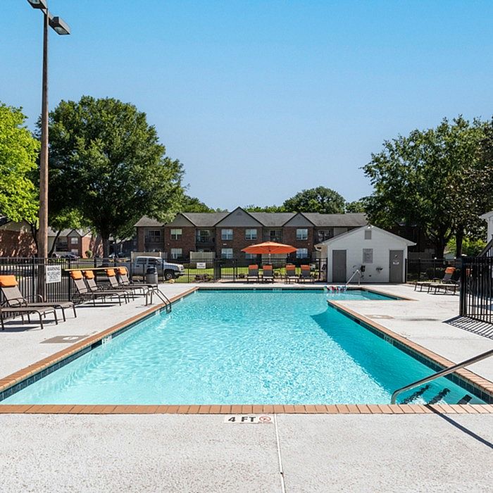 Sparkling clear pool surrounded by lounge chairs, nestled within a serene apartment community.