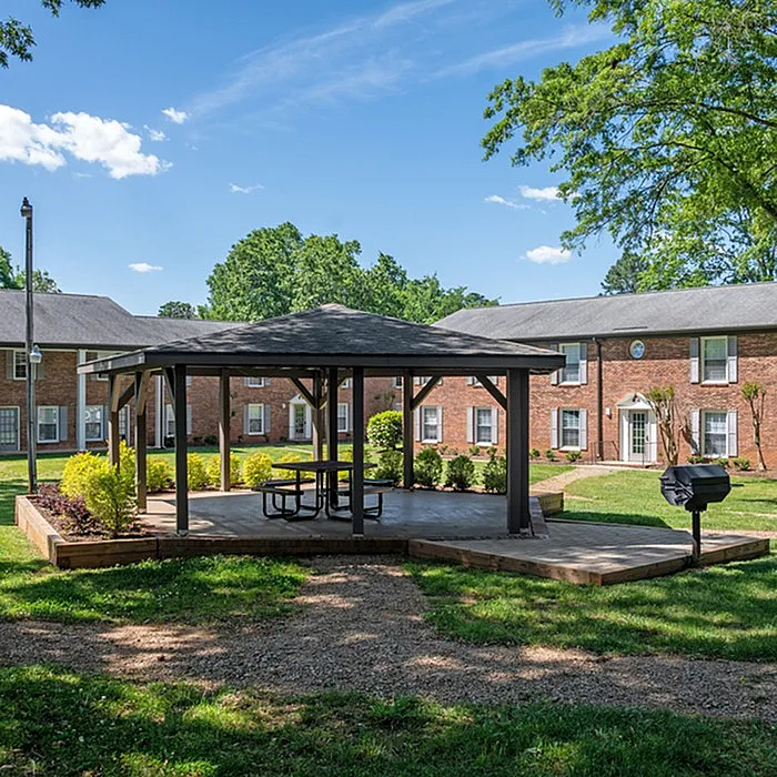 Inviting courtyard with a gazebo, surrounded by lush greenery and a red-brick apartment building.