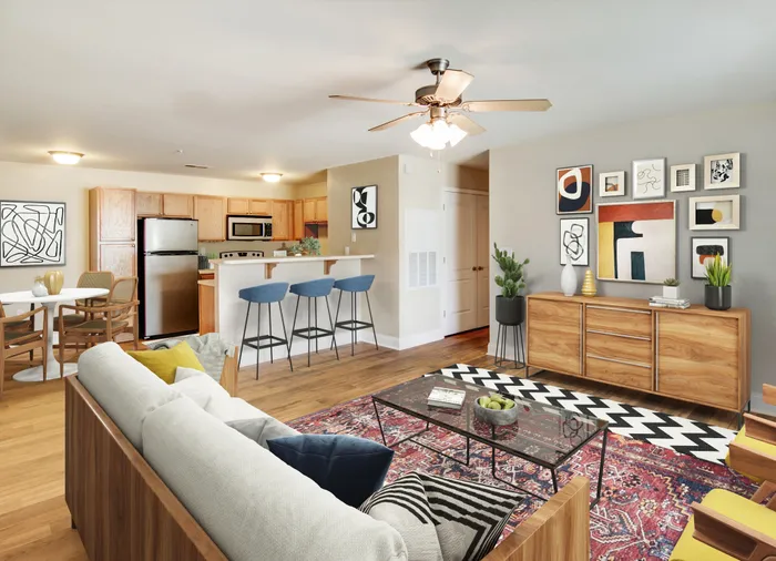 Stylish open-concept living room with modern decor, featuring a cozy sofa, vibrant rug, wooden flooring, and a sleek kitchen area.