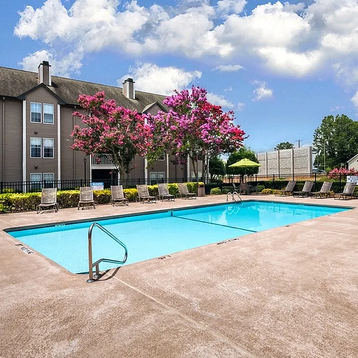 Charming apartment complex featuring a refreshing outdoor pool surrounded by blooming pink trees and lounge chairs, perfect for relaxation and outdoor enjoyment.